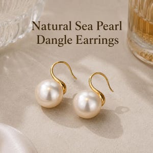 Könnte beinhalten: Ohrringe mit großen, weißen Naturperlen. Die Perlen hängen an geschwungenen, goldfarbenen Haken. Der Text "Natural Sea Pearl Dangle Earrings" ist über den Ohrringen zu sehen. Ein klassisches Schmuckstück.