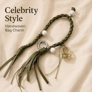 May include: A handwoven olive green bag charm featuring a braided cord, a silver-toned metal ring, a leather tassel, and white marbled beads. A faceted translucent yellow stone hangs from the cord. The text Celebrity Style Handwoven Bag Charm is visible.