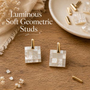 May include: Two square, geometric stud earrings with a mother-of-pearl mosaic design and gold-coloured posts. The earrings are displayed on a wooden surface, with additional gold-coloured earring posts and a small dish in the background. The text "Luminous Soft Geometric Studs" is visible.