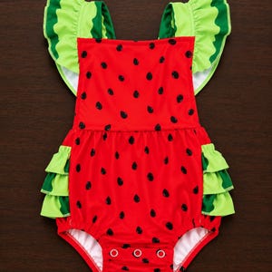 May include: A red romper featuring a black watermelon seed pattern, light green ruffled sleeves, and light green ruffled leg openings. The garment includes a gathered waistline and three silver-toned metal snap closures at the bottom crotch area.