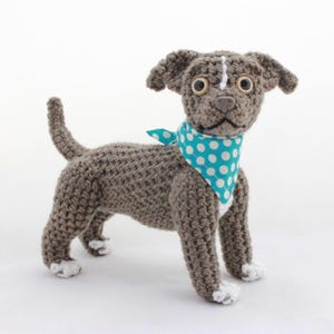 May include: A crocheted gray and white dog wearing a turquoise bandana with white polka dots. The dog has large brown eyes and a white patch on its forehead.