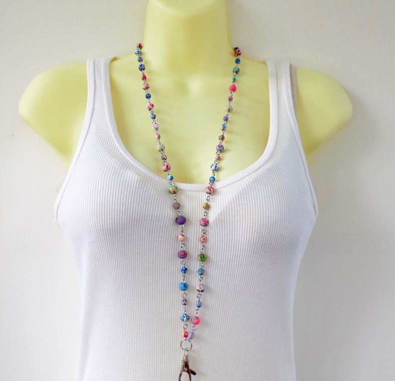 May include: A colorful beaded lanyard with a silver chain and a swivel clasp. The beads are made of various colors and patterns, including pink, blue, green, and purple.