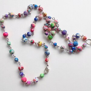 May include: A colorful beaded lanyard with a silver clasp. The beads are made of polymer clay and feature a variety of floral patterns in shades of pink, blue, green, and white.