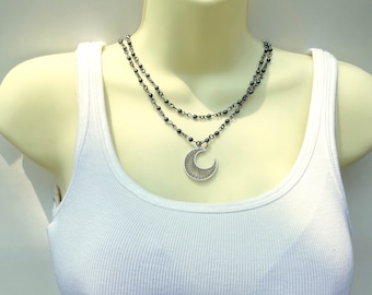 May include: A silver crescent moon pendant necklace with a delicate wire design hangs from a double strand of black beaded chain.