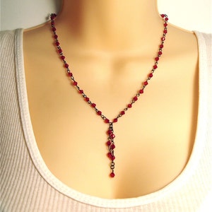 May include: A delicate necklace with a black chain and a dangling strand of red crystal beads.