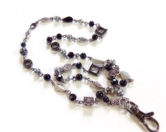 May include: A black and silver beaded lanyard with a silver clasp. The lanyard features black and silver beads, as well as silver charms.