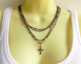 May include: A layered necklace with a cross pendant. The necklace features multiple chains and colorful beads.