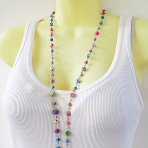 May include: A long silver chain necklace with colorful patterned beads. The beads are a mix of purple, blue, green, pink, and white.