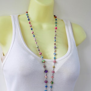 May include: A long multi-colored beaded necklace with a silver chain. The beads are made of fabric and are in shades of pink, blue, green, and purple.