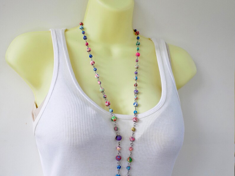 May include: A long multi-colored beaded necklace with a silver chain. The beads are made of fabric and are in shades of pink, blue, green, and purple.