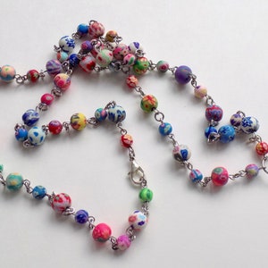 May include: A colorful beaded lanyard with a silver chain and a silver clasp. The beads are made of polymer clay and have a variety of floral patterns.