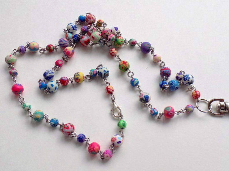 May include: A colorful beaded lanyard with a silver chain and a silver clasp. The beads are made of polymer clay and have a variety of floral patterns.