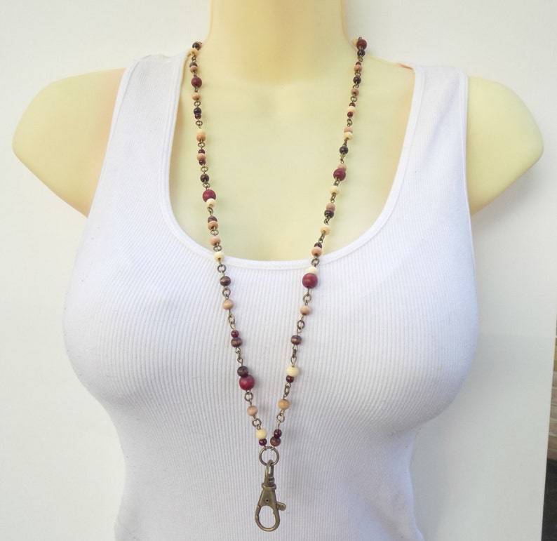May include: A long beaded lanyard necklace with a lobster clasp. The necklace features wooden beads in red, brown, and cream, strung with a metal chain. The clasp is bronze-coloured.