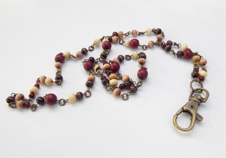 May include: A beaded lanyard with wooden beads in red, brown, and cream. The beads are strung on a bronze-coloured chain and finished with a bronze-coloured lobster clasp.
