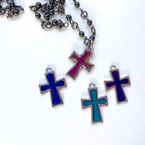 May include: A silver chain necklace with four different colored cross pendants. The crosses are blue, purple, teal, and pink.