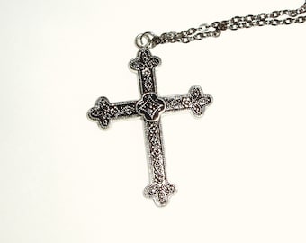Könnte beinhalten: Eine silberne Halskette mit einem detaillierten, verzierten Kreuz. Das Kreuz ist an einer silbernen Kette befestigt.