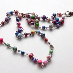 May include: A colorful beaded lanyard with a silver chain and a silver clip. The beads are made of polymer clay and have a variety of patterns and colors, including pink, blue, green, and white.