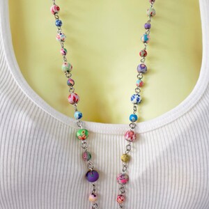 May include: A long silver chain necklace with colorful patterned beads. The beads are a mix of blue, green, pink, purple, and white.