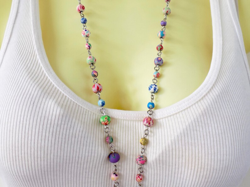 May include: A long silver chain necklace with colorful patterned beads. The beads are a mix of blue, green, pink, purple, and white.