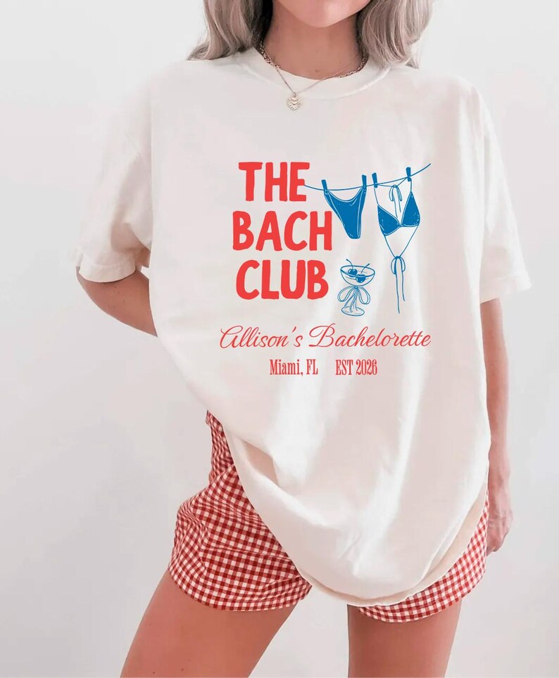 Bach Club bachelorette shirt with red and blue text, bikini and cocktail graphic, and personalized city and year trip details for matching bride crew outfits.