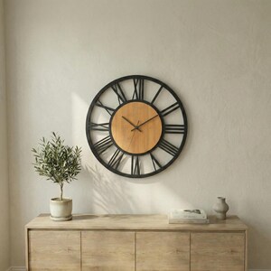 May include: A large, round wall clock with a black metal frame and Roman numerals. The clock face is a light brown wood, and the hands are black. The clock is mounted on a light-colored wall above a wooden cabinet.