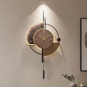 May include: A modern wall clock with a brown face and gold hands. The clock features a unique design with a semi-circular textured element and geometric shapes in black and gold. The clock is mounted on a light-colored wall.