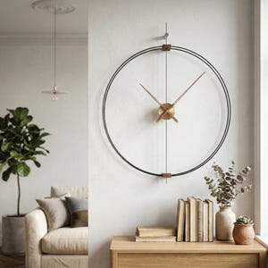 May include: A contemporary wall clock featuring a black metal frame and gold-toned hands. The clock has a minimalist design, with a circular shape. The clock is mounted on a white wall. The clock's diameter is approximately 76 cm.