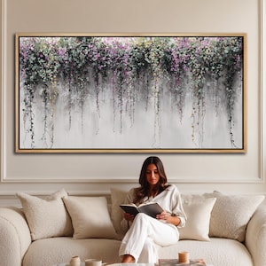 May include: A large rectangular floral painting with a gold frame. The artwork features cascading vines with purple, green, and white flowers against a light gray background. The painting is displayed above a cream-colored sofa.
