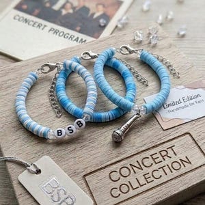 May include: Three bracelets made of light blue and white clay disc beads. One bracelet features white letter beads spelling BSB. Another bracelet includes a silver-toned microphone charm. Each bracelet has a silver-toned lobster clasp and chain.