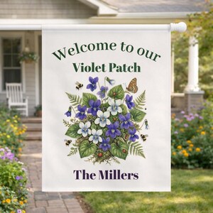 Może przedstawiać: Biała flaga ogrodowa z napisem "Welcome to our Violet Patch" i "The Millers" w kolorze ciemnozielonym i fioletowym. Flaga przedstawia kwiatową ilustrację fioletowych i białych fiołków, pszczół, motyla i biedronek.