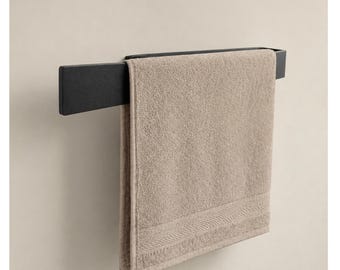 Puede incluir: Un toallero de metal negro sostiene una toalla beige doblada. La toalla tiene una superficie texturizada y un borde decorativo. El toallero está montado en una pared beige claro.