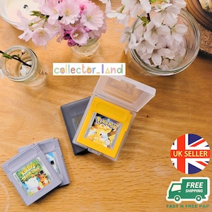 Op de afbeelding: Drie videospelcartridges voor een handheld console, waaronder een gele Pokemon-cartridge in een doorzichtig plastic hoesje en twee grijze Kirby's Dream Land-cartridges. De tekst collector_land is zichtbaar in het midden van de afbeelding.