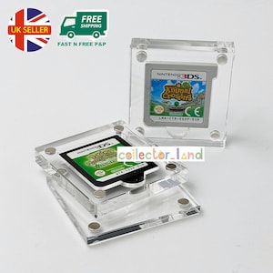 May include: Two clear acrylic display cases holding Nintendo 3DS and DS game cartridges. One case contains "Animal Crossing" and the other "Pokemon". The cases have magnetic closures and are designed to protect the game cartridges.