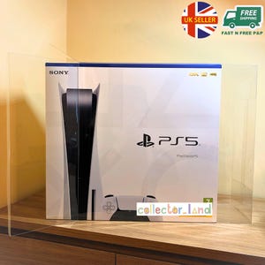 Könnte beinhalten: Eine weiße PlayStation 5 Konsolenbox mit schwarzen Akzenten, dem Sony-Logo und dem PS5-Logo. Die Box zeigt auch eine Controller-Grafik und den Text "PlayStation 5". Die Box wird in einer transparenten Schutzhülle präsentiert.