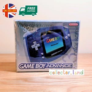 Puede incluir: Una Game Boy Advance azul oscuro en caja. La consola portátil tiene una pantalla a color ancha y gráficos de 32 bits. La caja presenta el logotipo de Game Boy Advance y la marca Nintendo. El texto "Wide color screen" es visible.