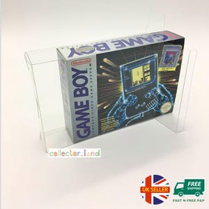 Puede incluir: Una caja del sistema de videojuegos Game Boy en una vitrina de plástico transparente. La caja presenta el logotipo de Nintendo y las palabras "GAME BOY COMPACT VIDEO GAME SYSTEM". La ilustración muestra una consola Game Boy con un cartucho de juego.