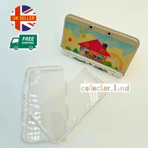 May include: A Nintendo 3DS console with a colourful house and rainbow design, alongside a clear protective case. The console has a beige top with a cartoon illustration. The clear case is open, showing the interior.
