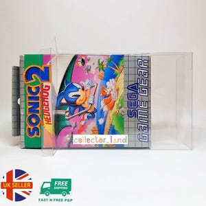 May include: A SEGA Game Gear video game cartridge for Sonic the Hedgehog 2, in a clear protective case. The game box features Sonic and Tails on a tropical background. The text "SONIC 2 HEDGEHOG" is visible on the box.