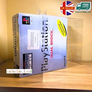 May include: A boxed PlayStation Dual Shock video game console, protected by a clear plastic case. The box is predominantly white and blue, featuring the PlayStation logo and the words "DUAL SHOCK". It also includes the text "Free Demo Disc Inside Featuring SoundScope".