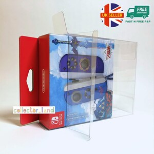 Puede incluir: Un par de Joy-Con de Nintendo Switch en una caja con una cubierta de plástico transparente. Los Joy-Cons son azules y blancos con detalles dorados. La caja tiene el texto "The Legend of Zelda" y "Joy-Con Pair".