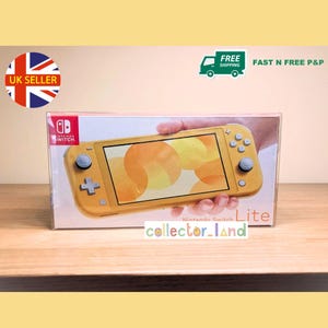 May include: A yellow Nintendo Switch Lite console in its original packaging. The box features the Nintendo Switch logo and the word "Lite". The screen displays an orange and yellow graphic. The text "collector_land" is visible.