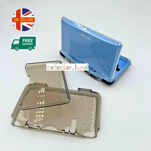 Puede incluir: Una consola Nintendo DS Lite azul claro con una funda protectora transparente. La funda está hecha de plástico transparente y está diseñada para proteger la consola de arañazos y daños. La imagen también muestra una funda protectora separada y abierta.