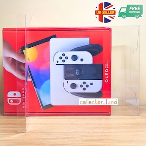 Puede incluir: Una consola Nintendo Switch modelo OLED en su caja roja original, exhibida dentro de una funda de plástico transparente. La consola es blanca y negra, con mandos blancos. La caja tiene el logo de Nintendo y el texto "OLED Model".