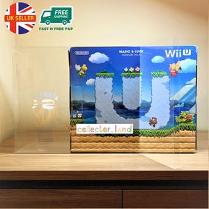 May include: A Nintendo Wii U Premium Pack box with Mario & Luigi graphics, encased in a clear protective display. The box art shows a classic video game level with floating platforms and characters. The text "collector_land" is visible.