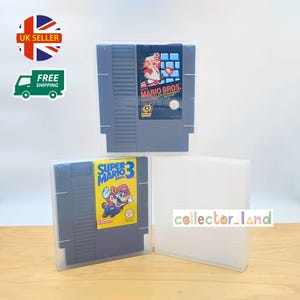 以下が含まれることがあります： 透明なプラスチックケースに入った3つのNintendo Entertainment System（NES）ゲームカートリッジ。2つのカートリッジには、「スーパーマリオブラザーズ」と「スーパーマリオブラザーズ3」を含むカラフルなゲームラベルが付いています。ケースは薄茶色の表面にあります。