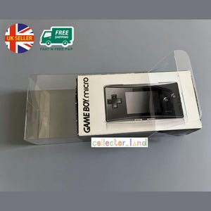 May include: A boxed Game Boy Micro console. The box is white with the words "GAME BOY Micro" printed on it. The console is black with a small screen and control buttons. The packaging is in a clear plastic case. The box has a UK seller sticker.