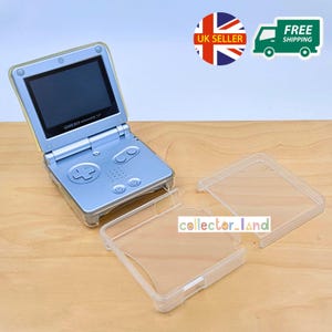May include: A silver Game Boy Advance SP handheld console with a clear protective case. The console is open, showing the screen. The case is in two parts. The text "GAME BOY ADVANCE SP" is visible.