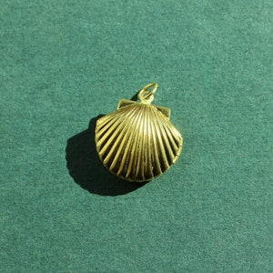 May include: A gold-colored seashell pendant charm. The seashell is detailed with ridges and has a loop at the top for attaching to a necklace or bracelet.