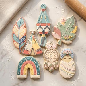 May include: A collection of decorated sugar cookies in a bohemian theme. The cookies include a feather, a hanging plant, a leaf, a teepee, a sloth with a dreamcatcher, a rainbow, and a baby. The cookies are decorated with pastel colors.