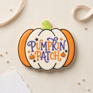 May include: A pumpkin-shaped sugar cookie decorated with white, orange, and green icing. The center features the purple and orange text "PUMPKIN PATCH" surrounded by small orange stars, black stars, and two tiny orange pumpkin illustrations.